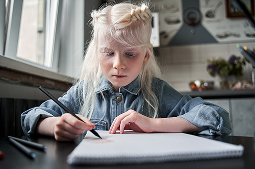 Child with albinism writing in a notebook